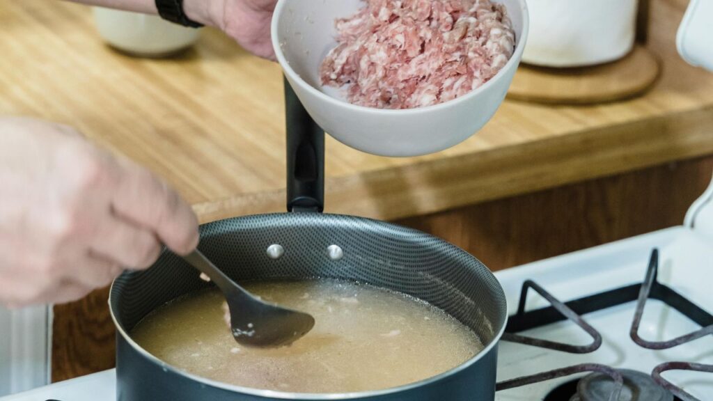 Hand mixing Leggs seasoning into ground pork in a metal bowl