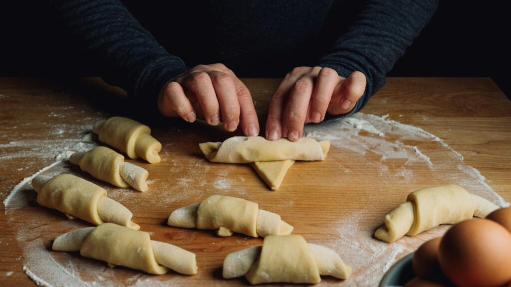 Process shots of rolling ensaimada dough into a thin sheet and coiling it into a snail shape.